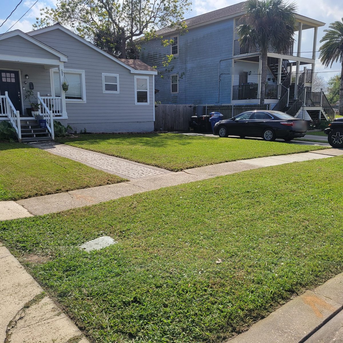 A green front lawn either side of a paver walkway leading to the porch steps of a gray raised cottage.